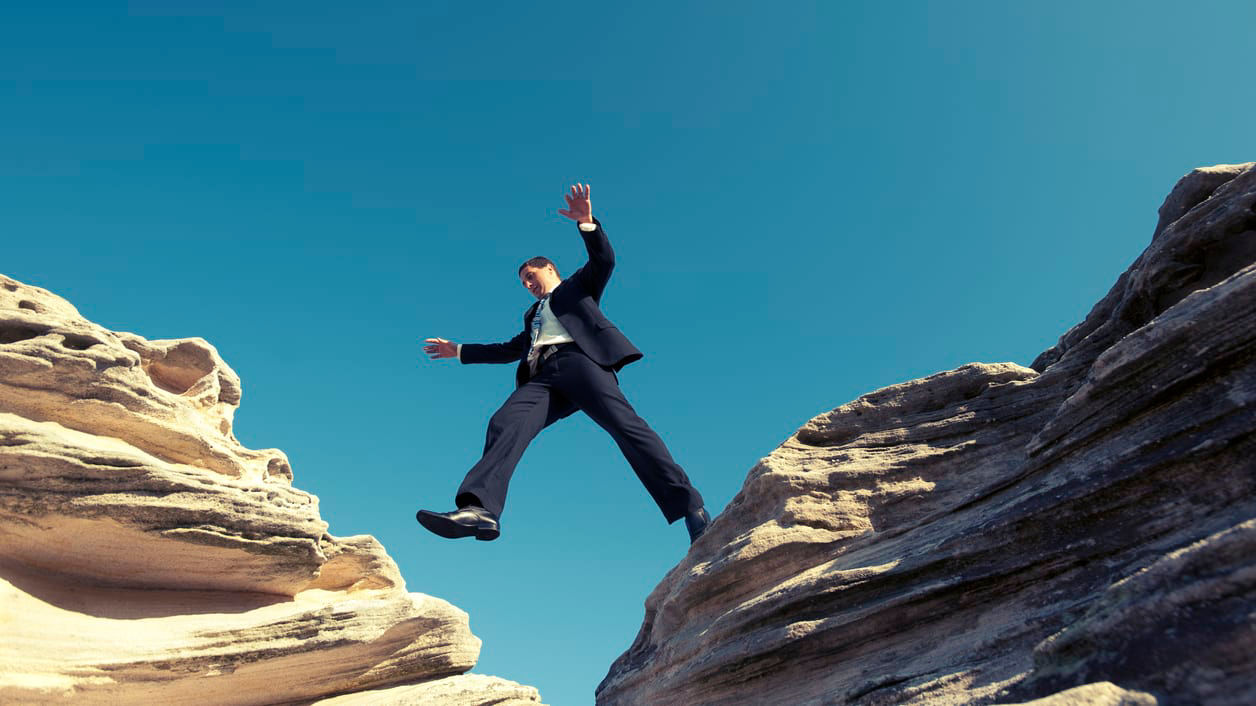 A businessman jumping over a cliff.