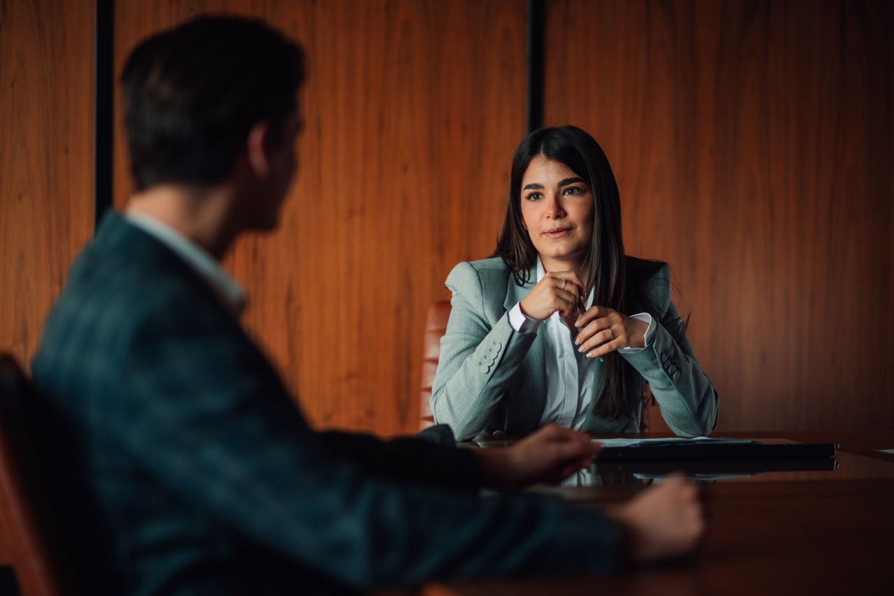 Two professionals engaged in an interview, conversing at a long corporate table.
