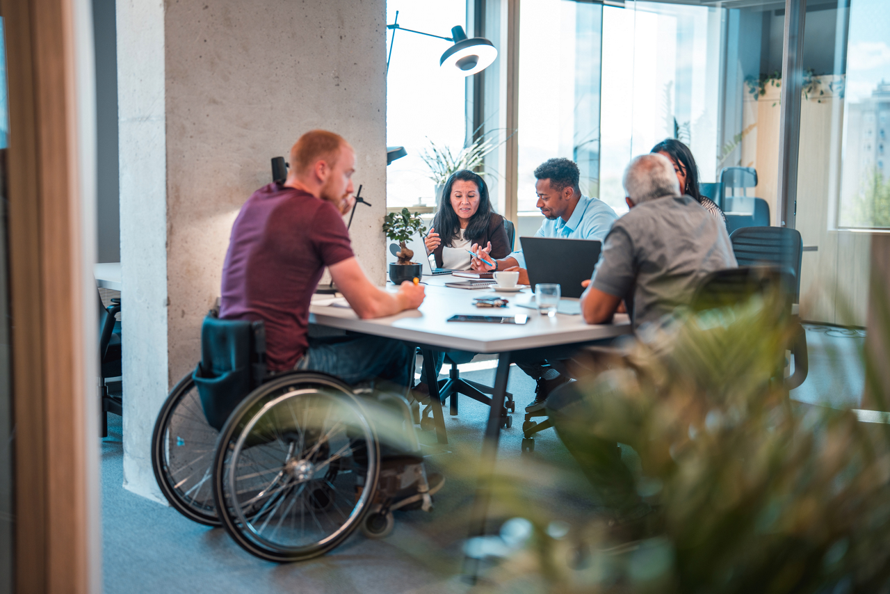 Indoor full body shot of disabled Caucasian, Latin and multi-ethnic coworkers at an open concept office. They are seated in comfortable chairs as they work using laptops.