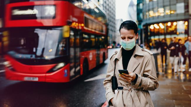 A woman wearing a face mask in front of a double decker bus in london.