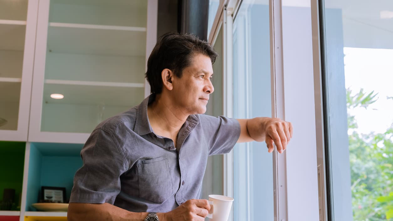 A man looking out a window with a cup of coffee.