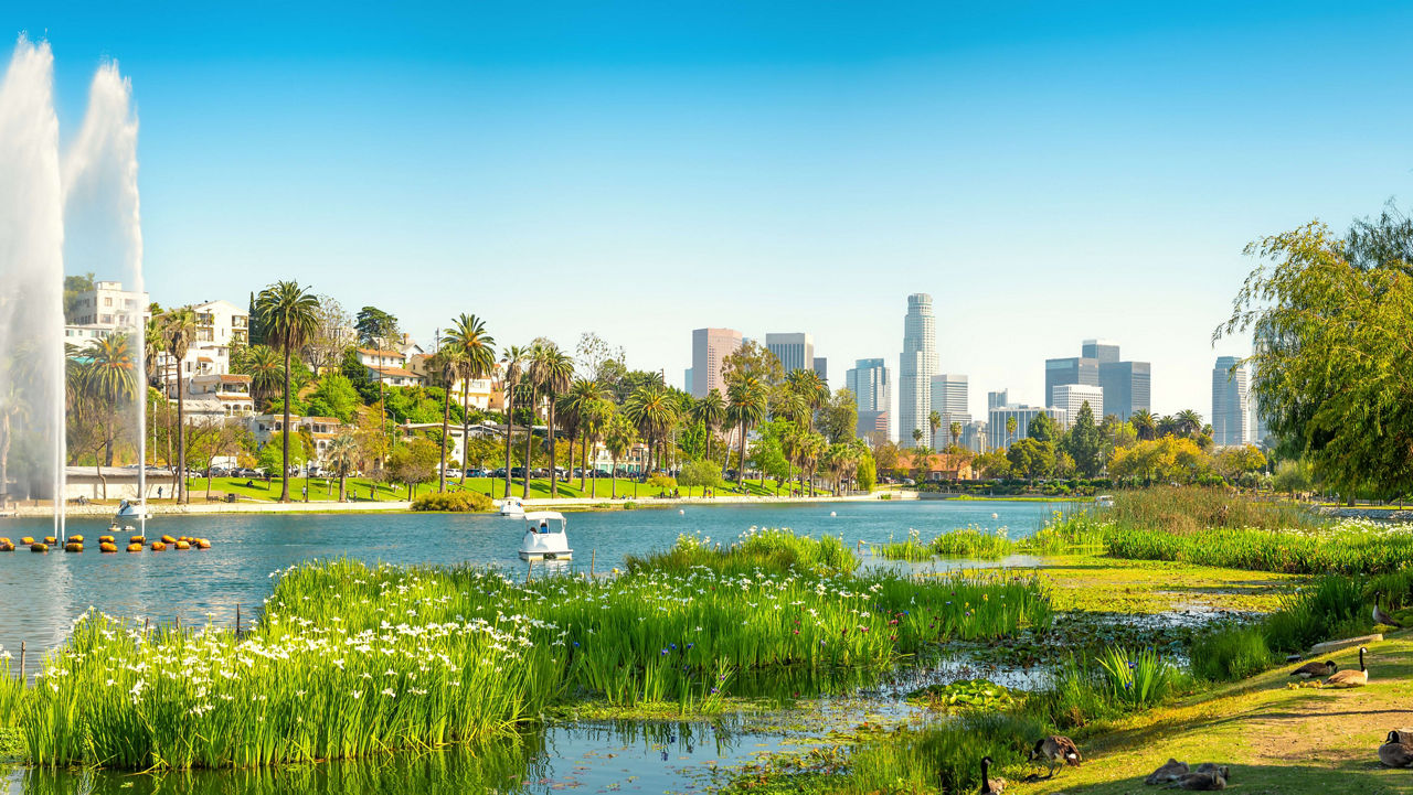 A park with two fountains on the left, a lake and Los Angeles' skyline in the distance.