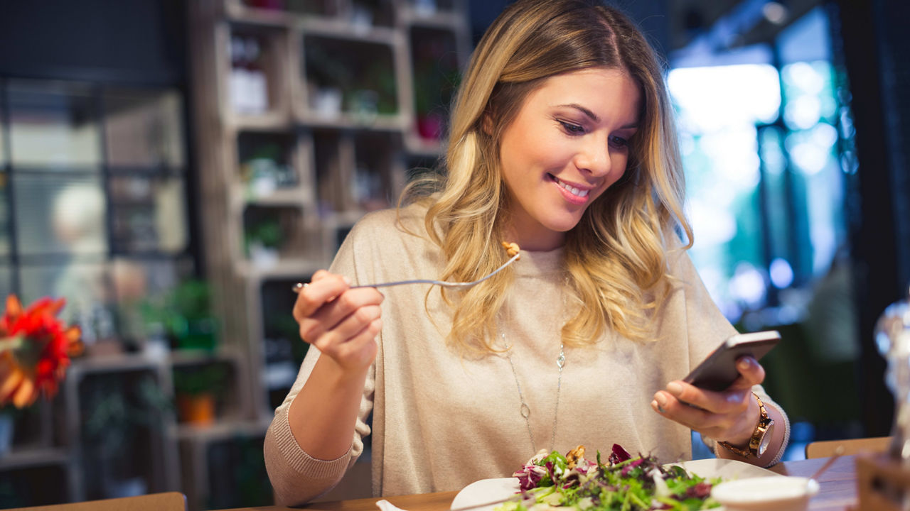 A woman looking at her phone while eating a salad.