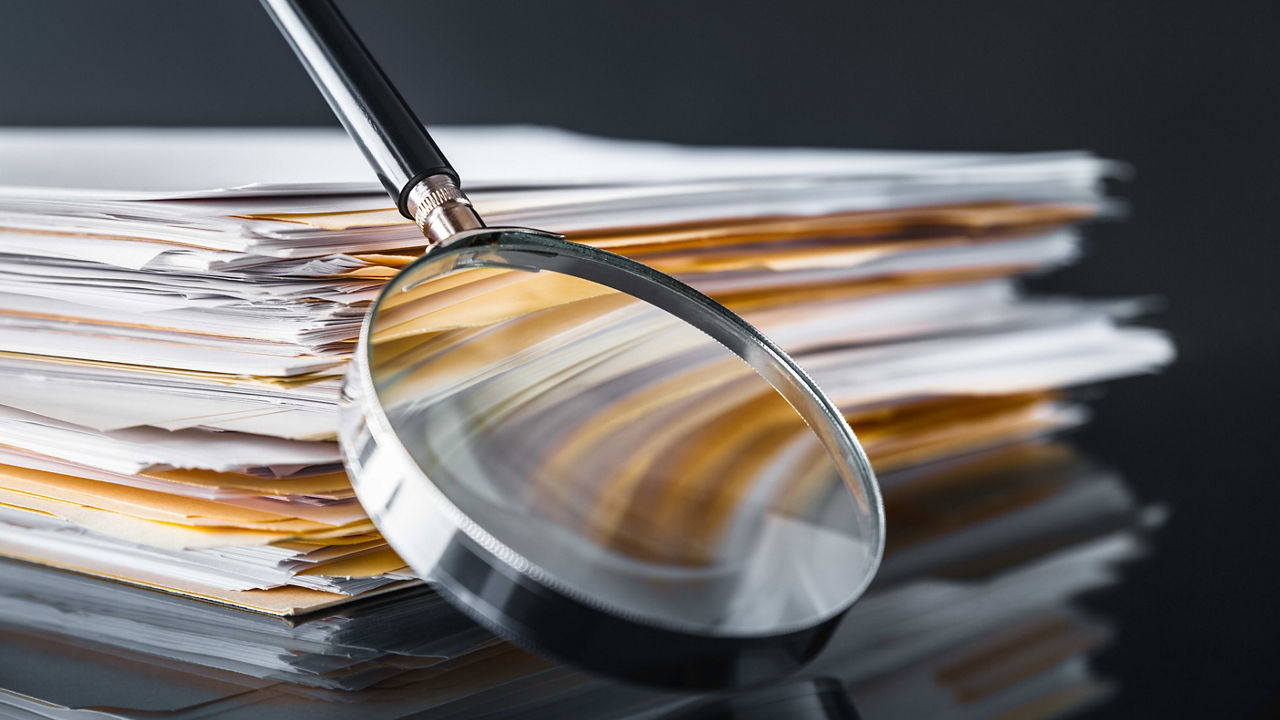 A magnifying glass on top of a stack of documents.