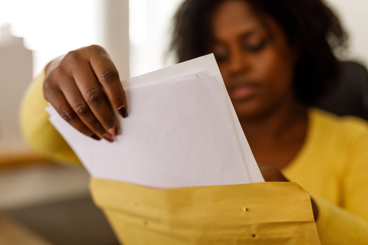 Selective focus shot of diligent young woman sitting at her desk at the office and packing documents in a yellow envelope.