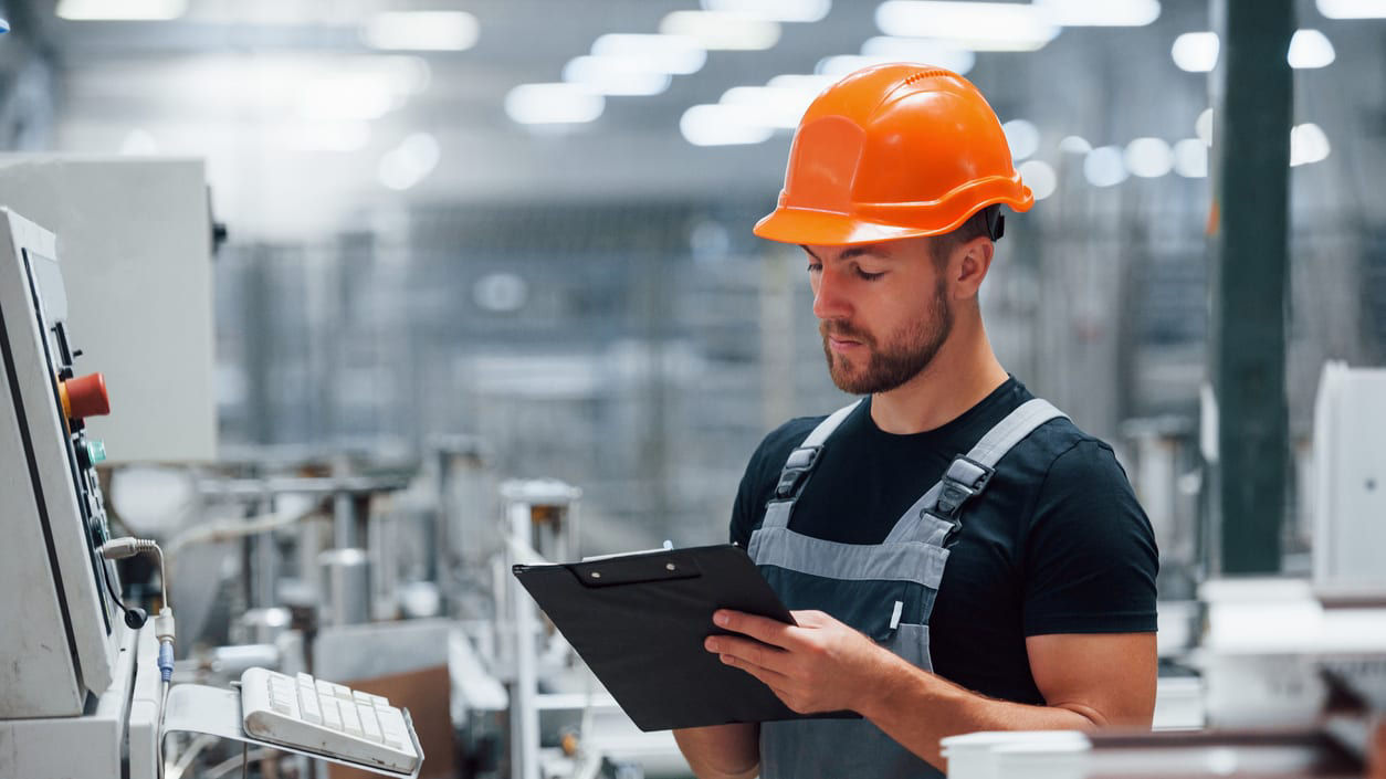 A worker in a factory holding a clipboard.