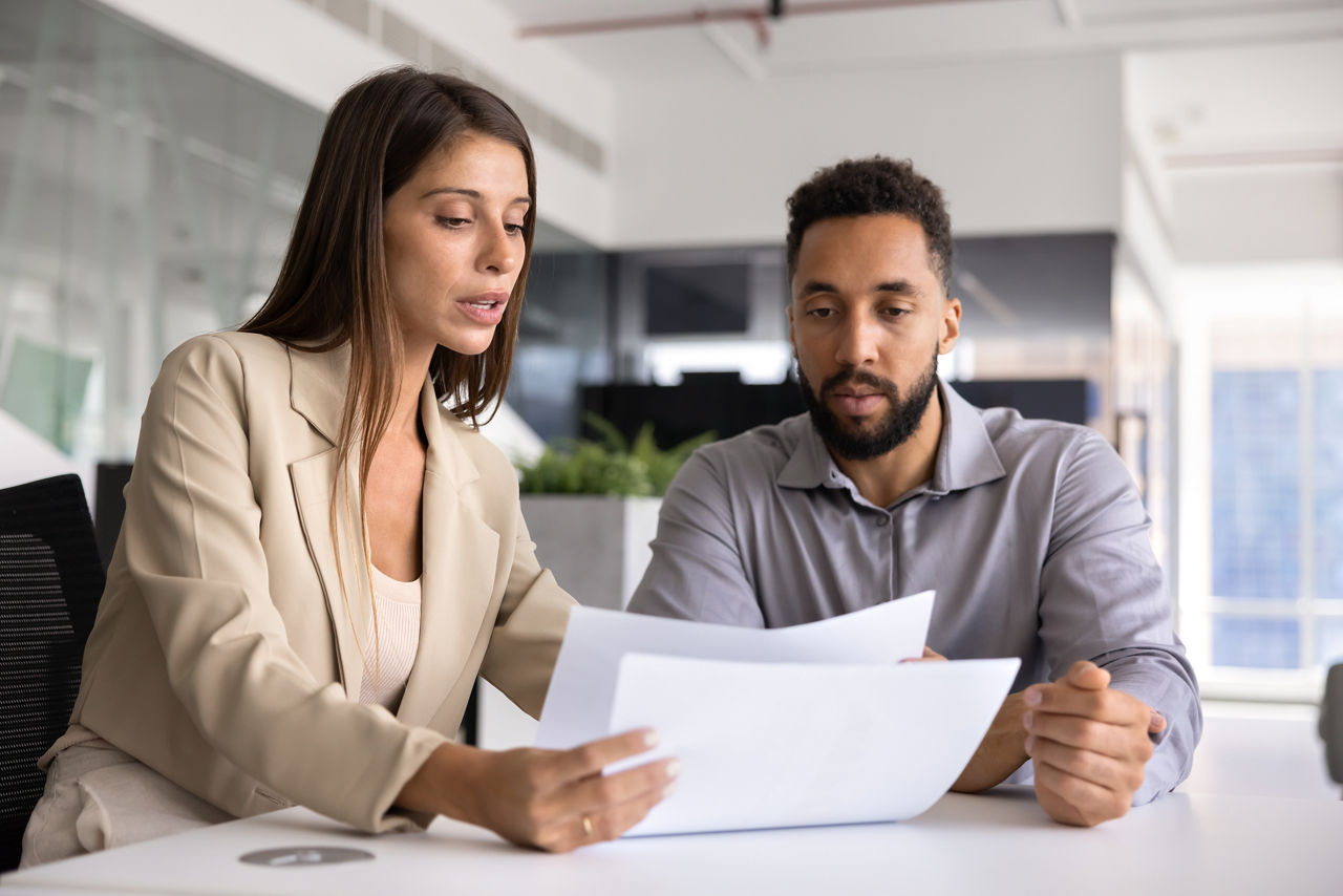 Female manager holding papers sitting at table while coaching team member on right