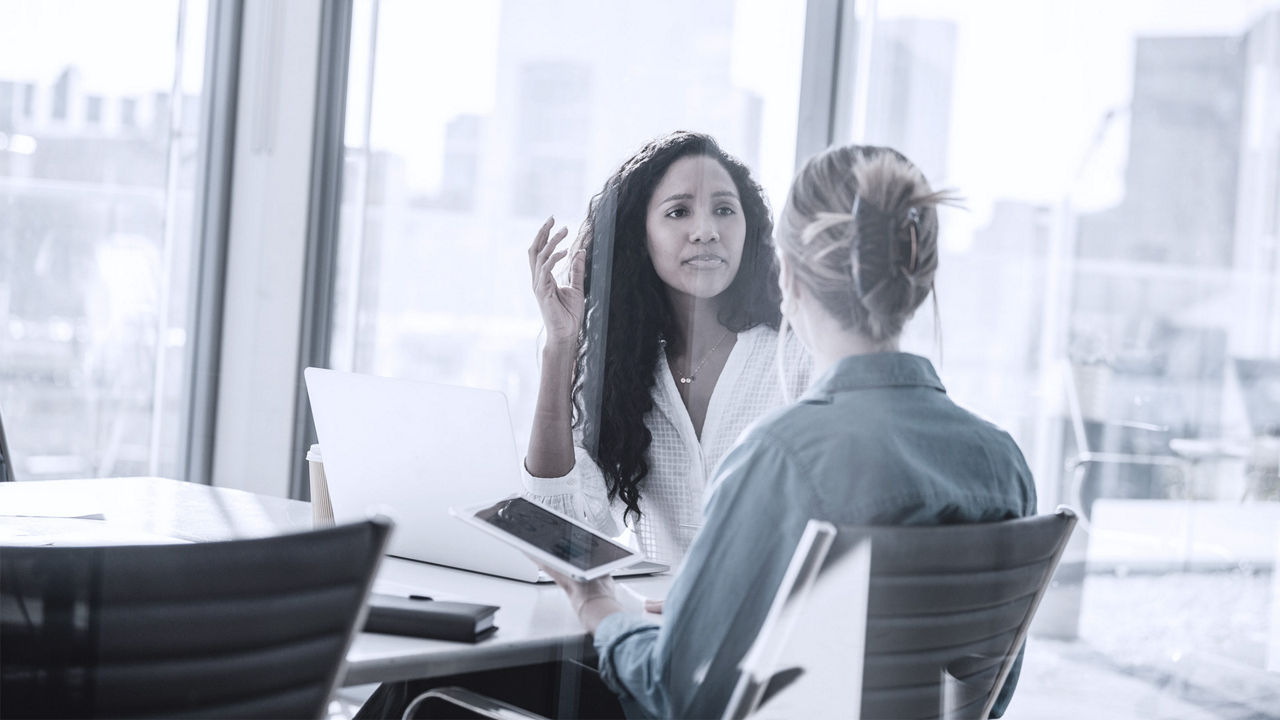 Manager talking to employee, sitting around office table in conference room