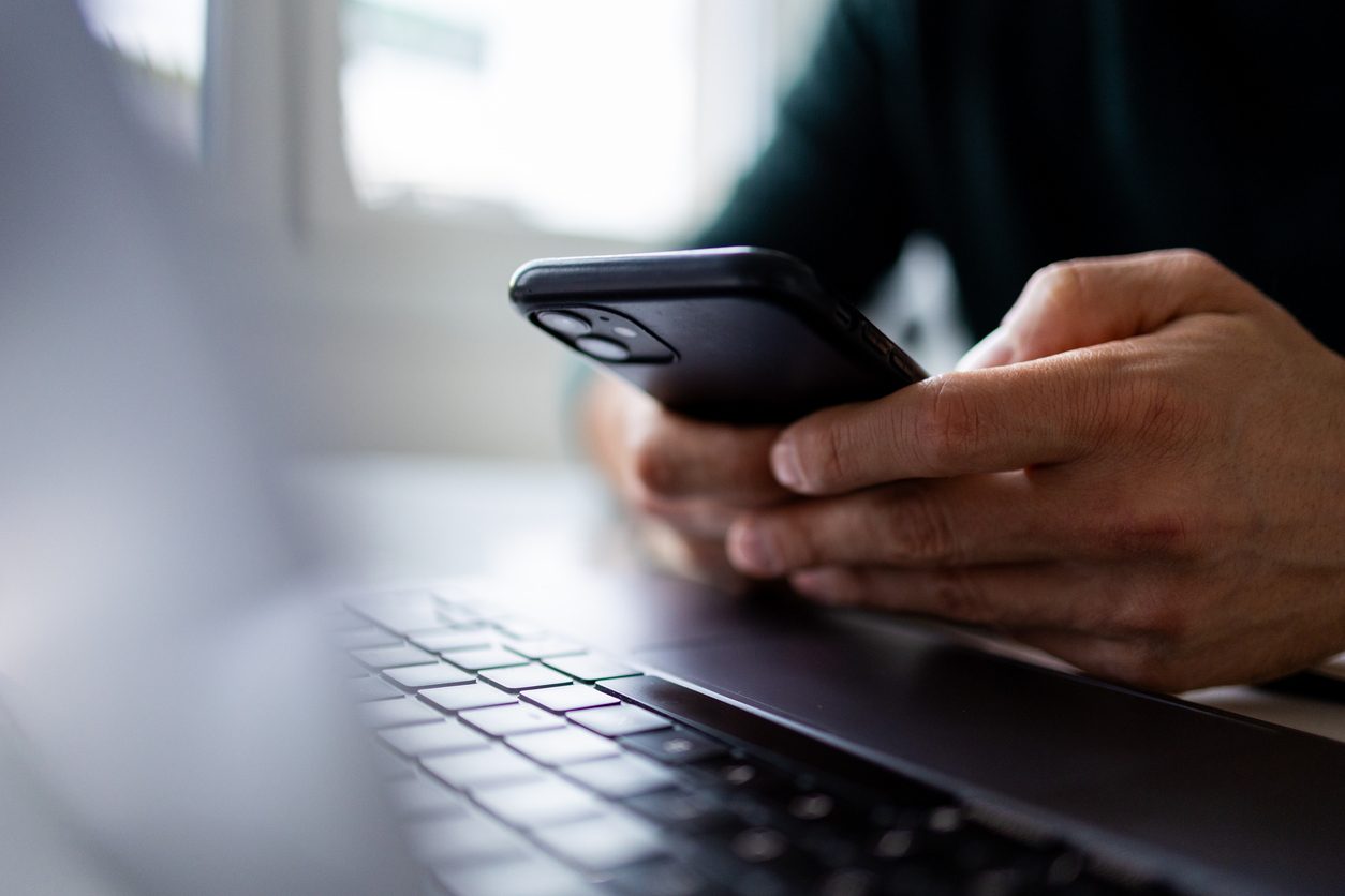 closeup on a man at his laptop holding his smart phone