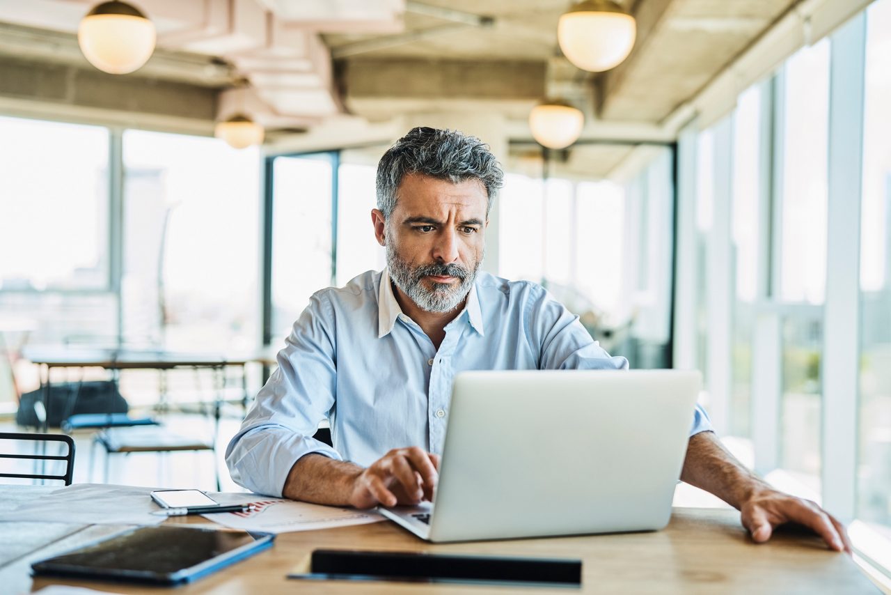 Mature businessman using laptop at table. Confident male entrepreneur is working at coworking space. He is wearing shirt.