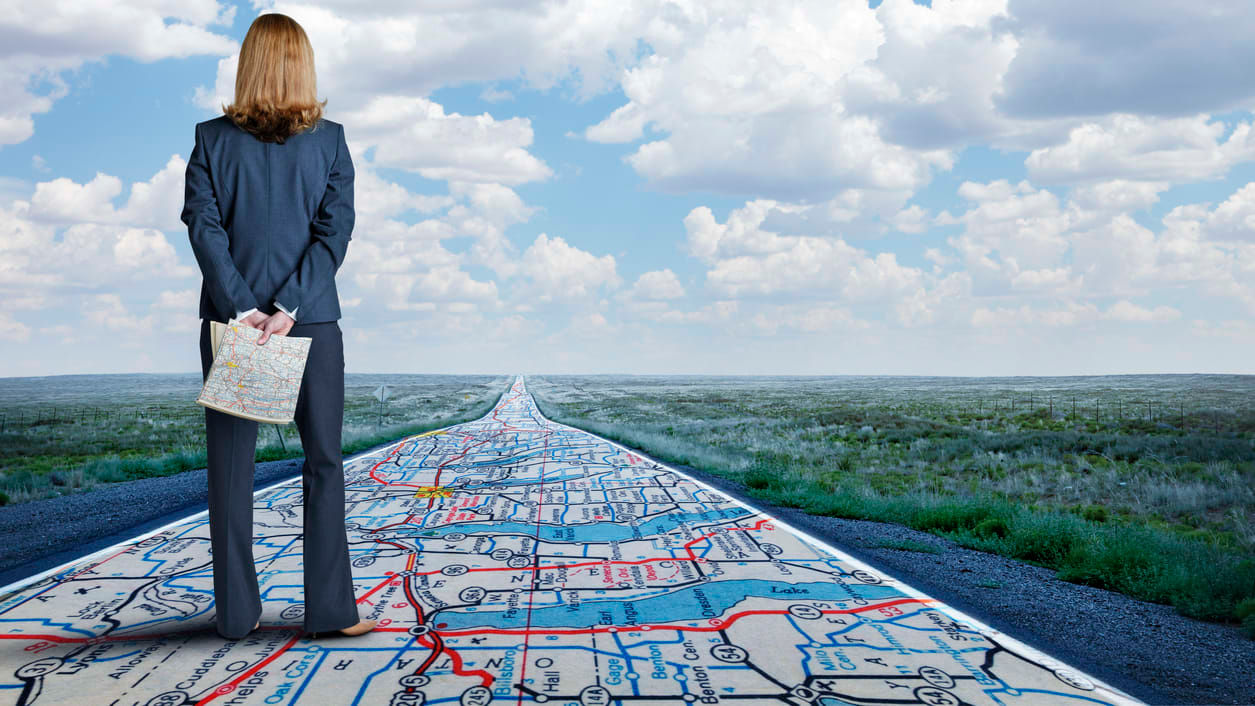 A business woman standing on a road with a map.