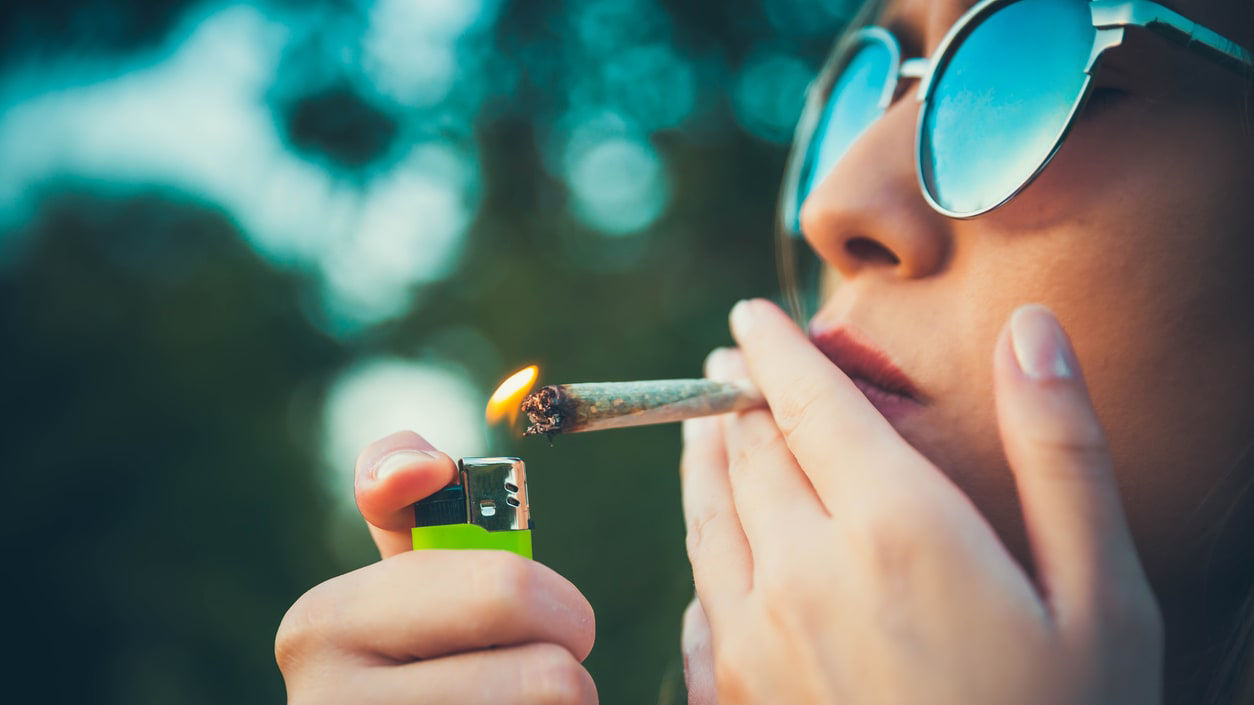 A woman wearing sunglasses is smoking a lighter.