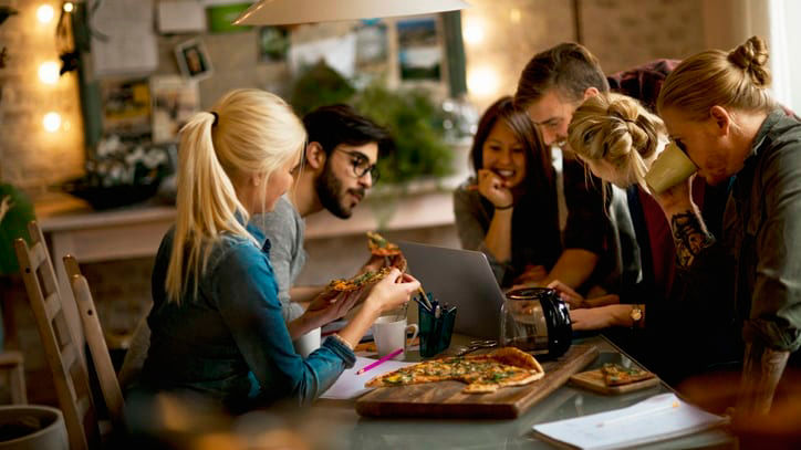 A group of people sitting around a table eating pizza.
