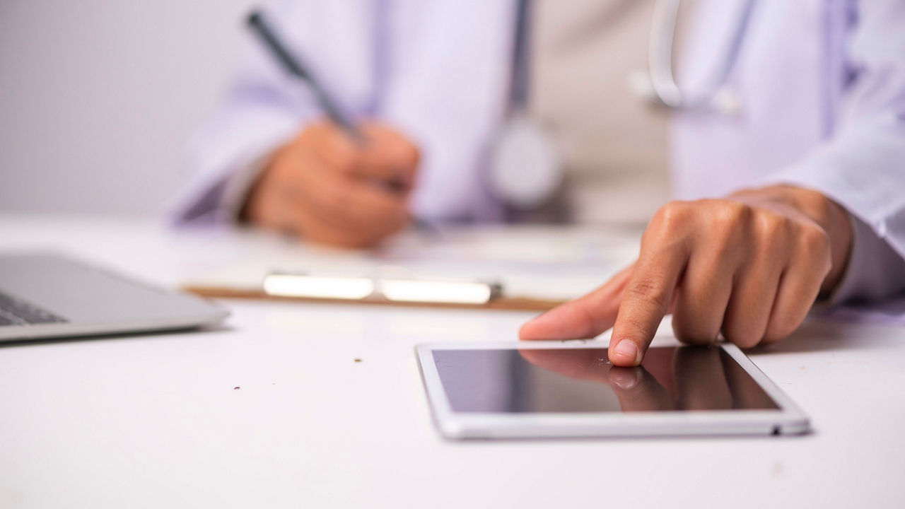 A female doctor is using a tablet computer at a desk.