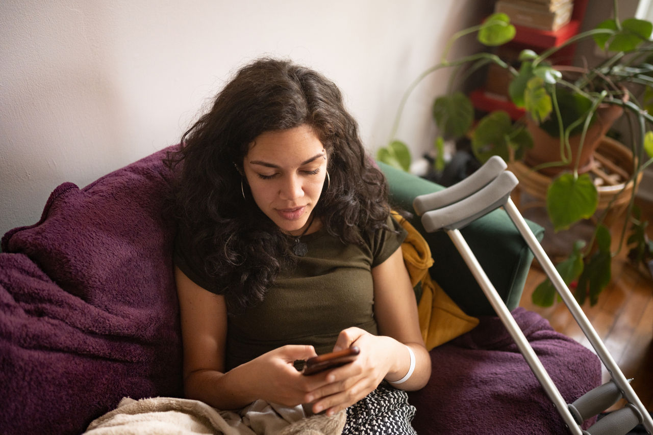 This is a photograph from a high angle view of an injured millennial Puerto Rican woman texting while resting at home in Chicago.