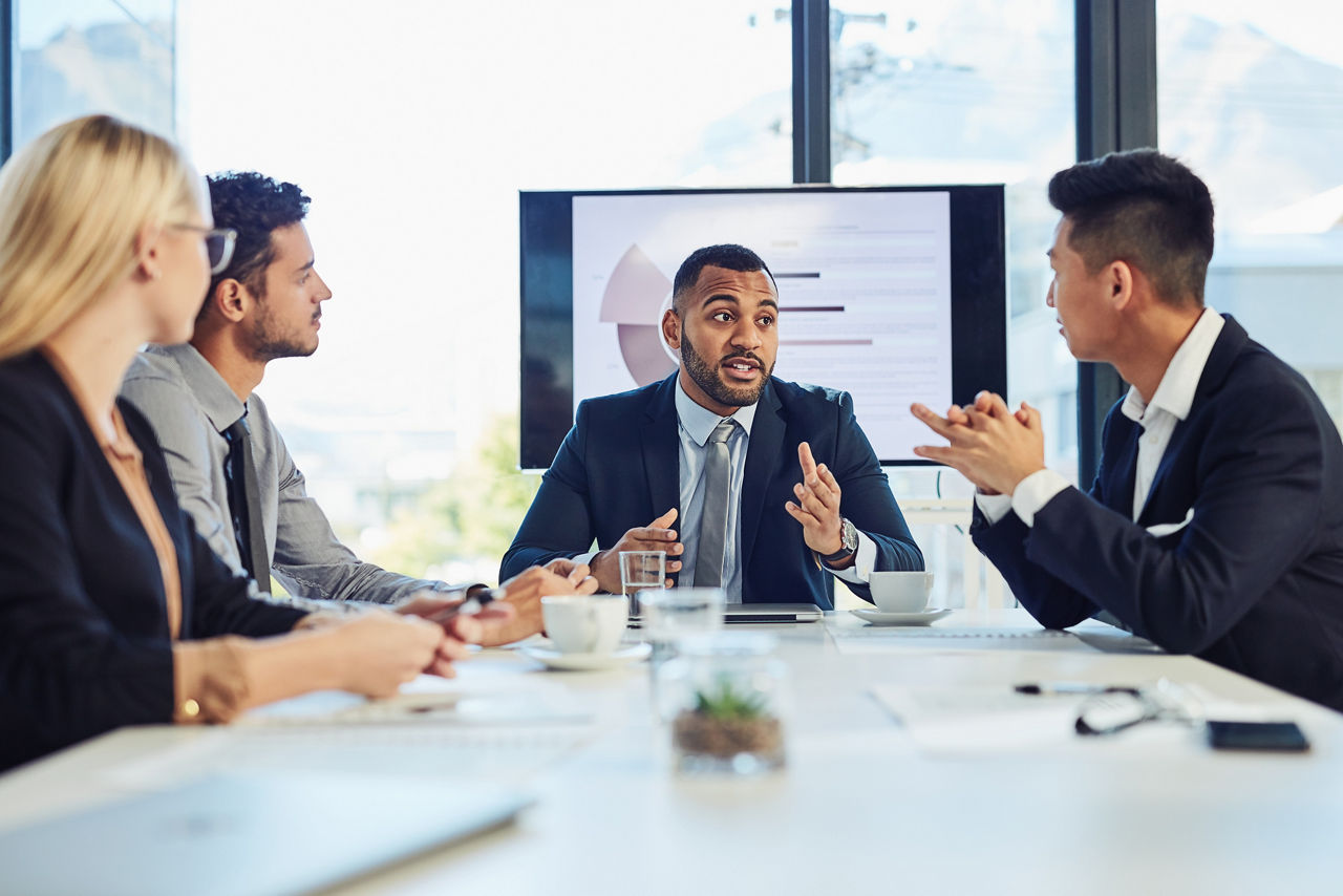 Male executive sitting at end of table talking to three leaders