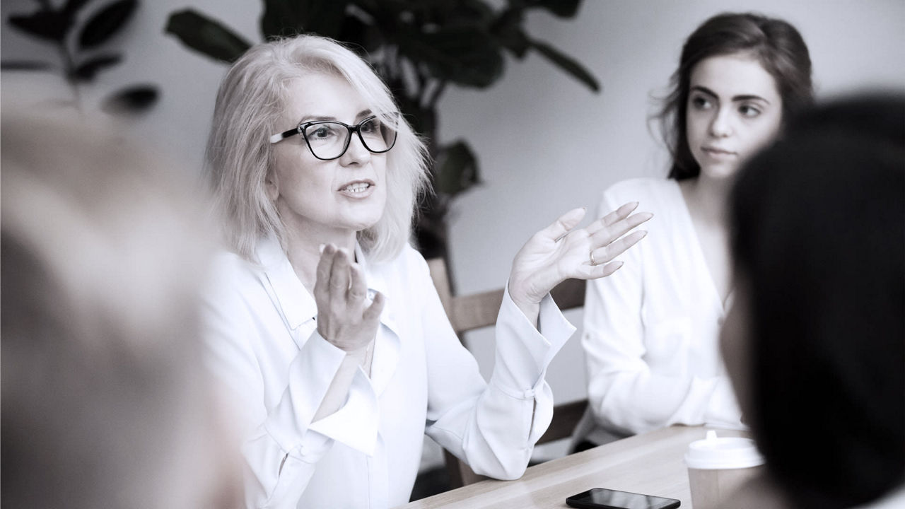A group of women sitting at a table talking to each other.