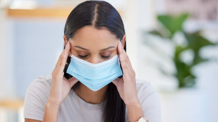 A woman wearing a surgical mask while working on her laptop.