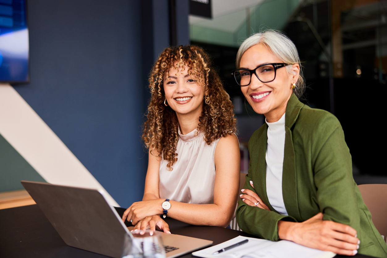 Young office worker in her 20s and businesswoman in her 40s in office using computer, collaboration, teamwork, meeting