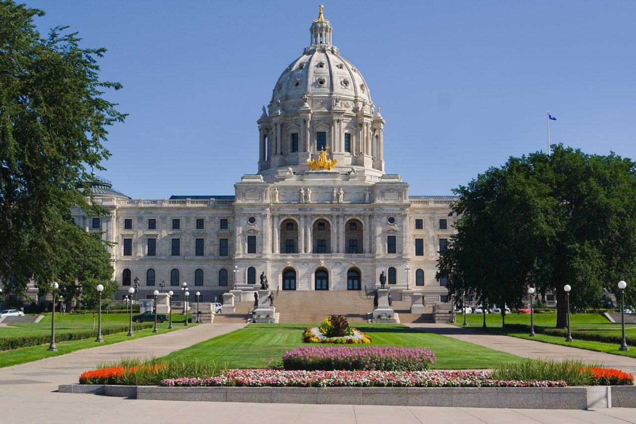 Front entrance approach of the Minnesota State Capitol building in St. Paul, Minn. The architectural classical style of the monumental domed building exterior facade, formal gardens, flower beds, lawns and grounds are a tourist travel destination.