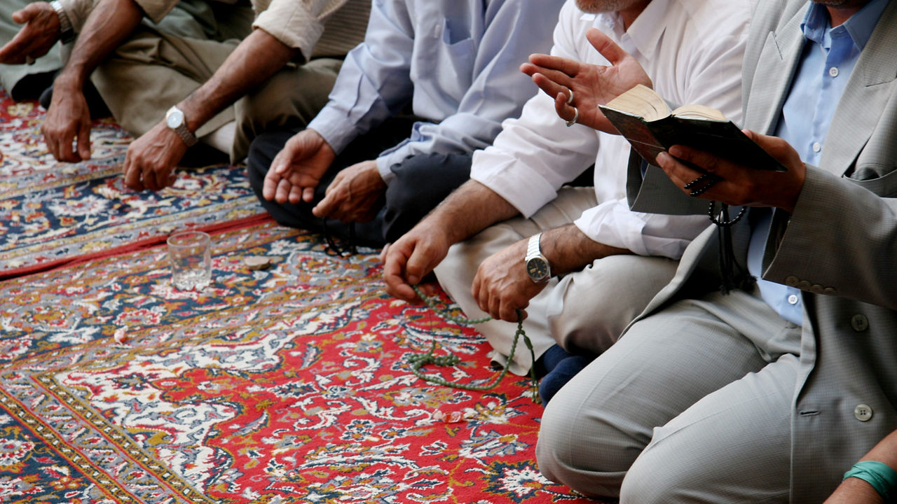 A group of men praying on a rug.