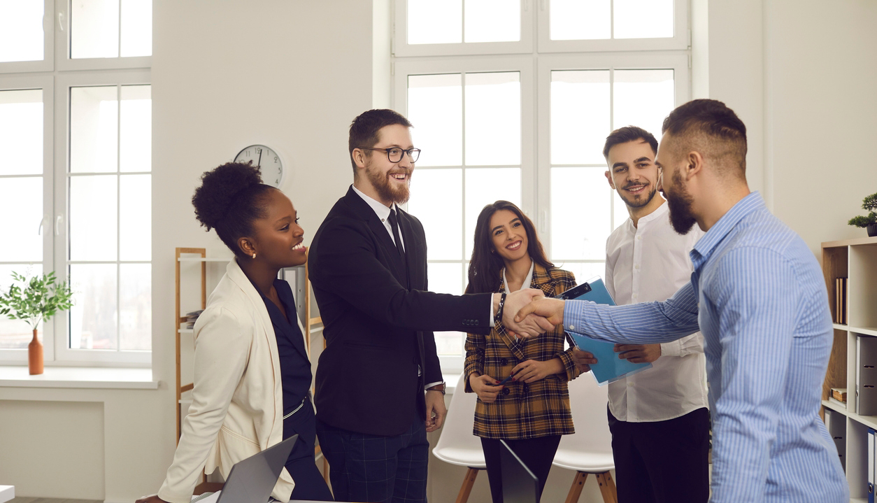 People in a business meeting. Male leader of a multiracial business team greets a new team member shaking his hand. Concept of business relationships, hiring and promotion.
