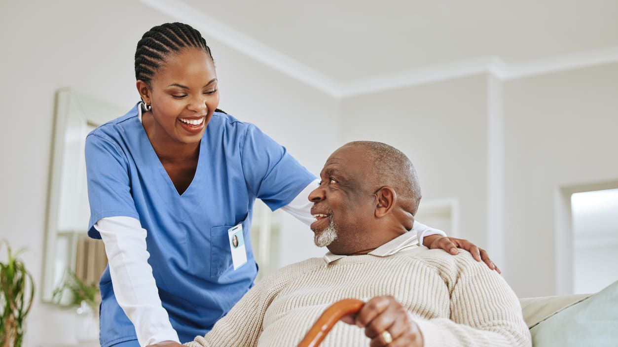 A nurse is helping an elderly man with a cane.