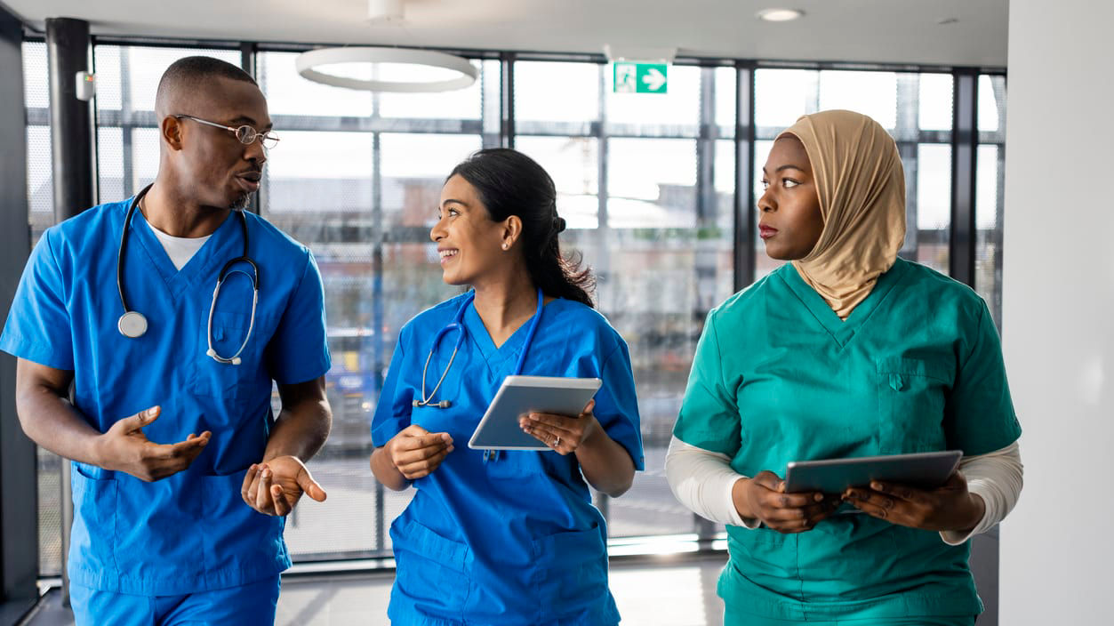 A group of nurses are walking down a hallway with a tablet in their hands.