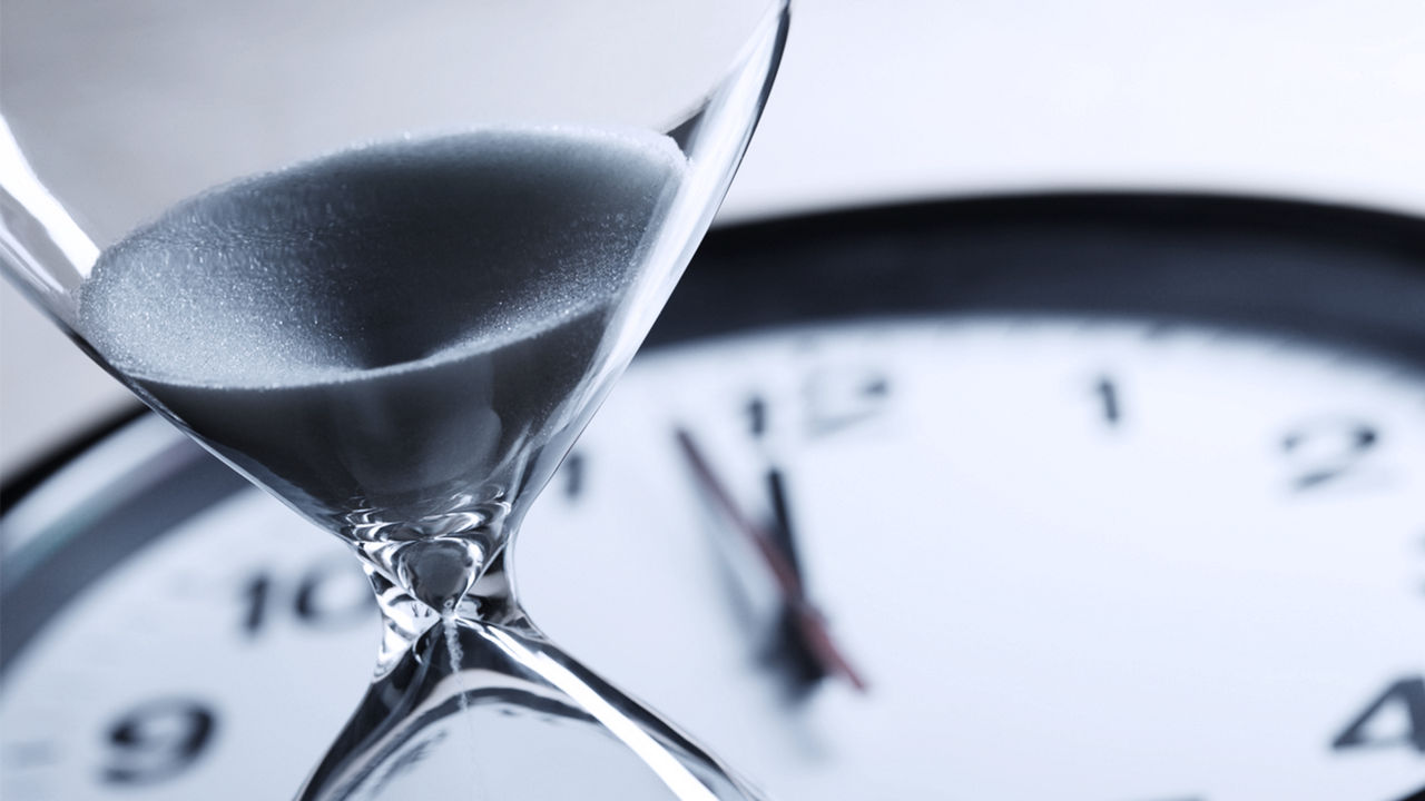 An hourglass in the foreground and clock in the background.