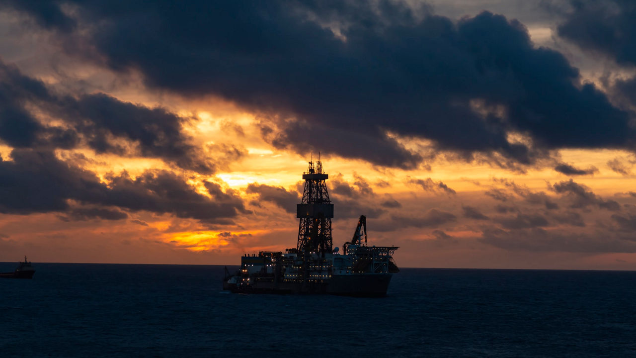 An oil rig in the middle of the ocean at sunset.