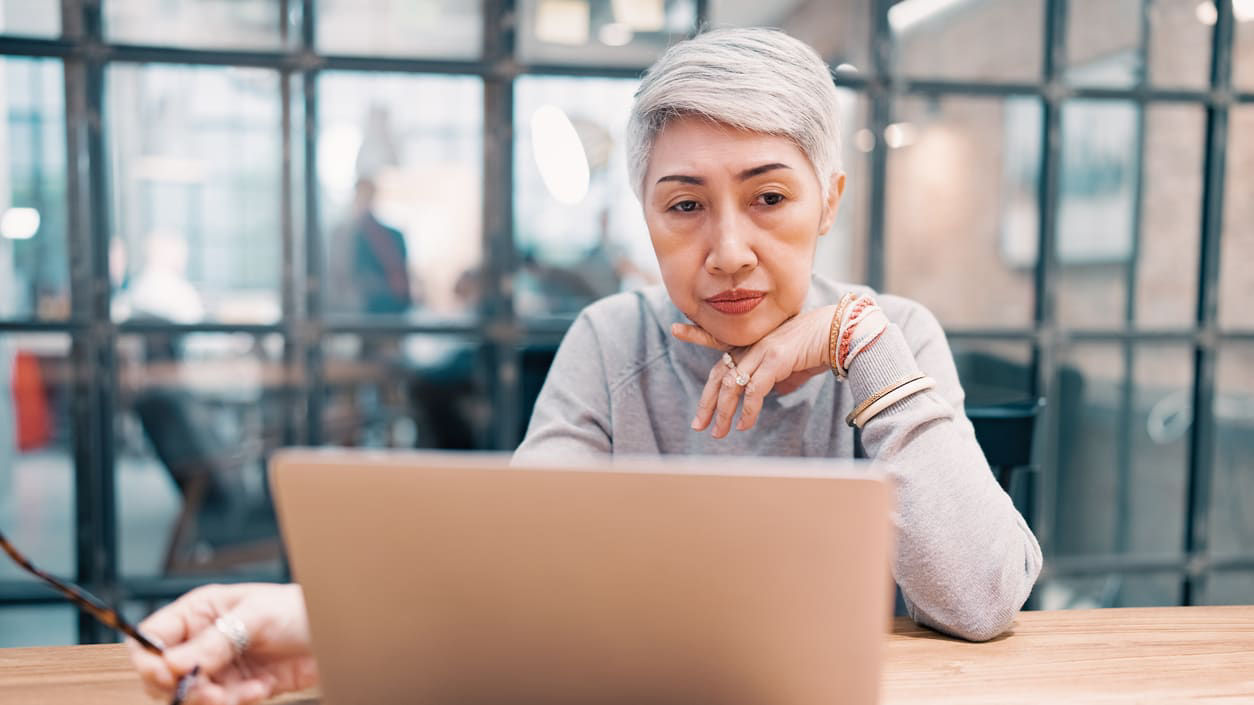 An older woman looking at her laptop at a table.
