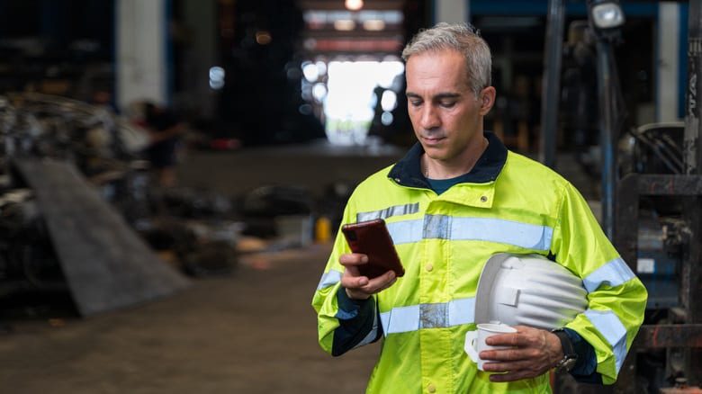 A blue collar worker with hard hat off, using his cellphone.