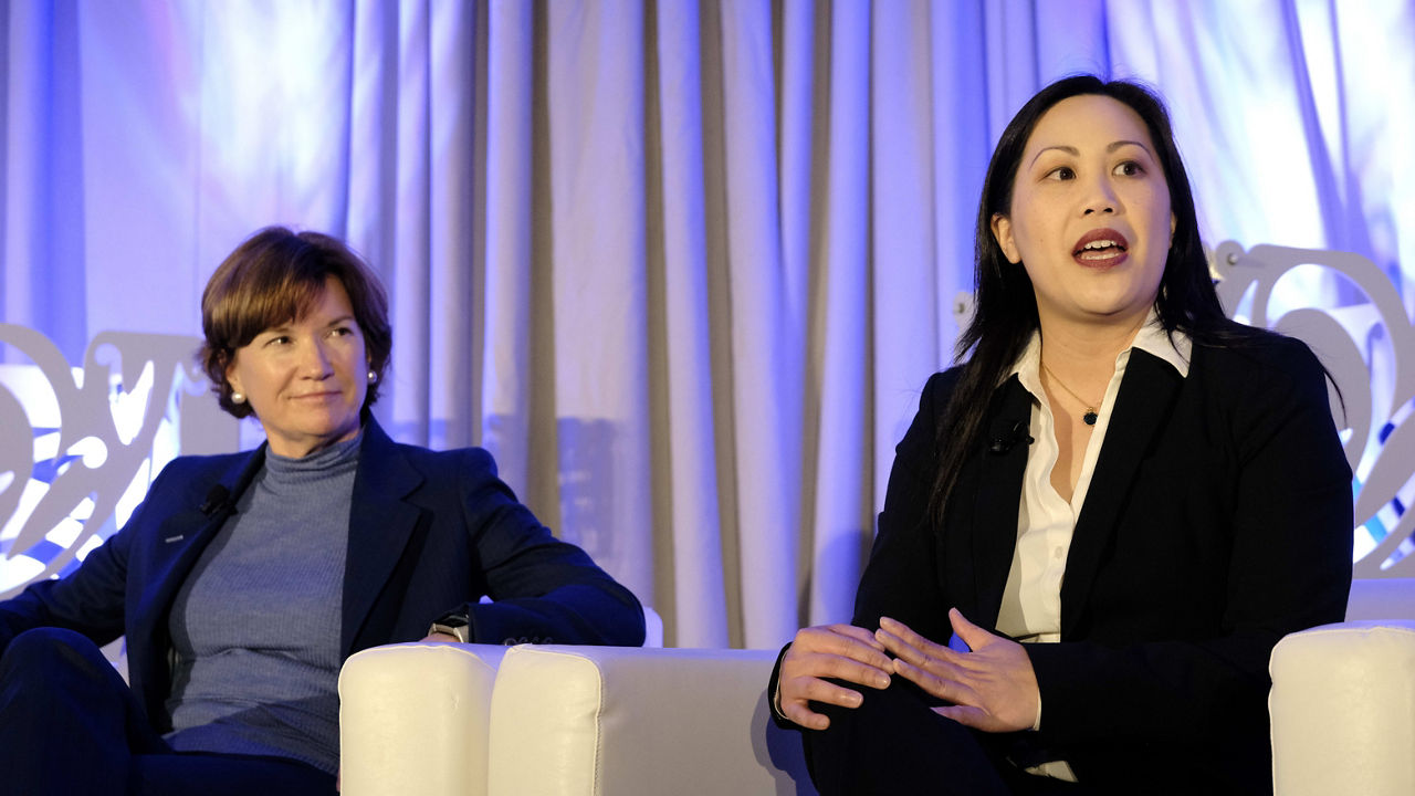 Two women sitting on a white chair in front of a white background.
