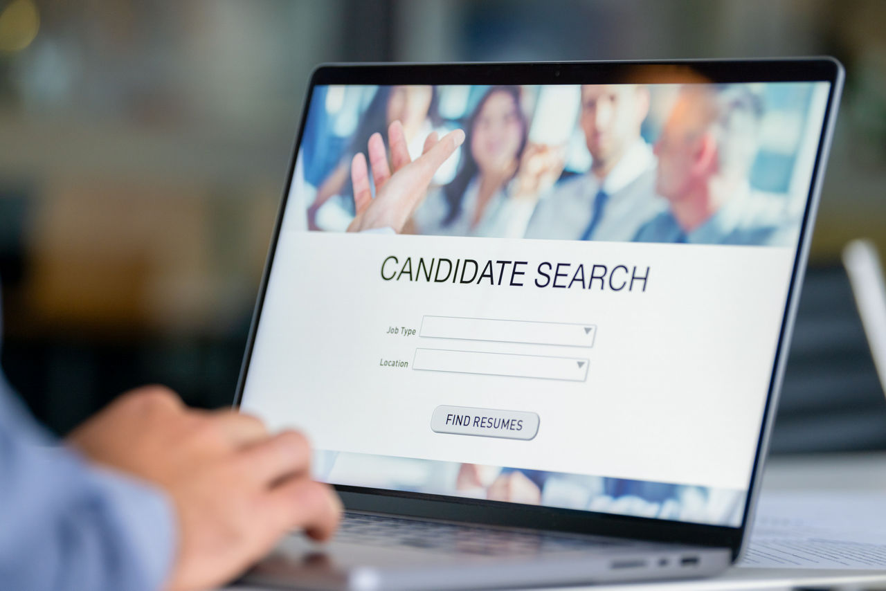Close up of a Businessman looking at recruitment website on a laptop computer. Candidate search page with job type and location buttons. The mans hands can seen working on a keyboard.