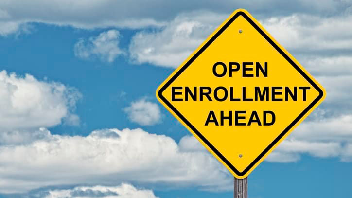A yellow sign that says open enrollment ahead against a cloudy sky.