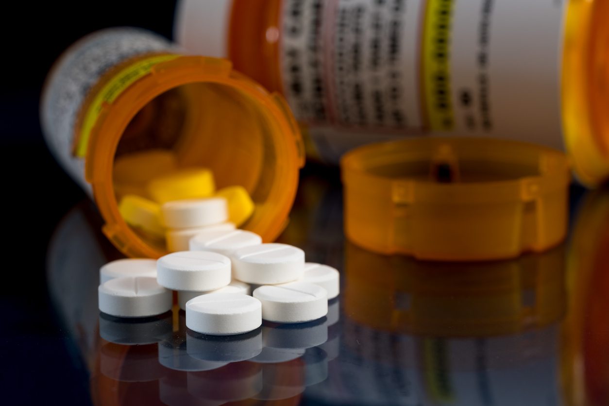 Prescription bottle of oxycodone and pills on a glass table with reflections