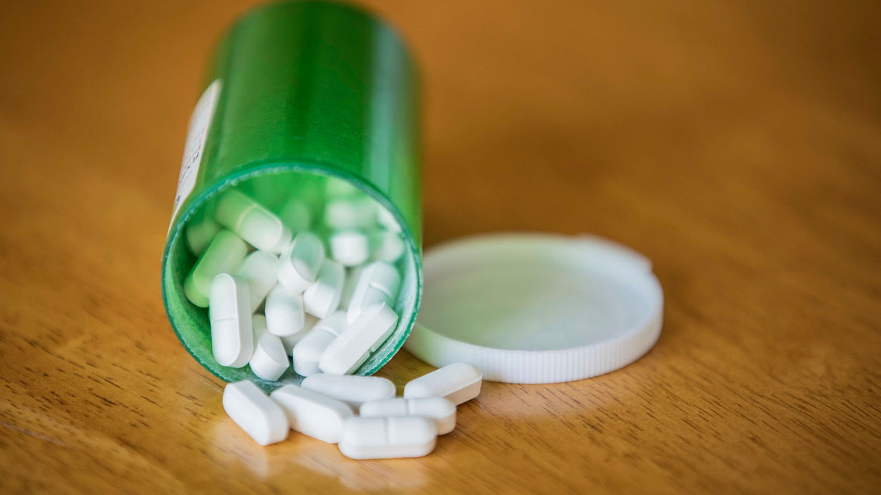 A green pill bottle with white pills spilling out on a wooden table.