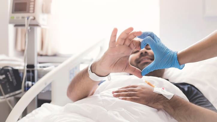A man laying in a hospital bed with a blue glove on his hand.