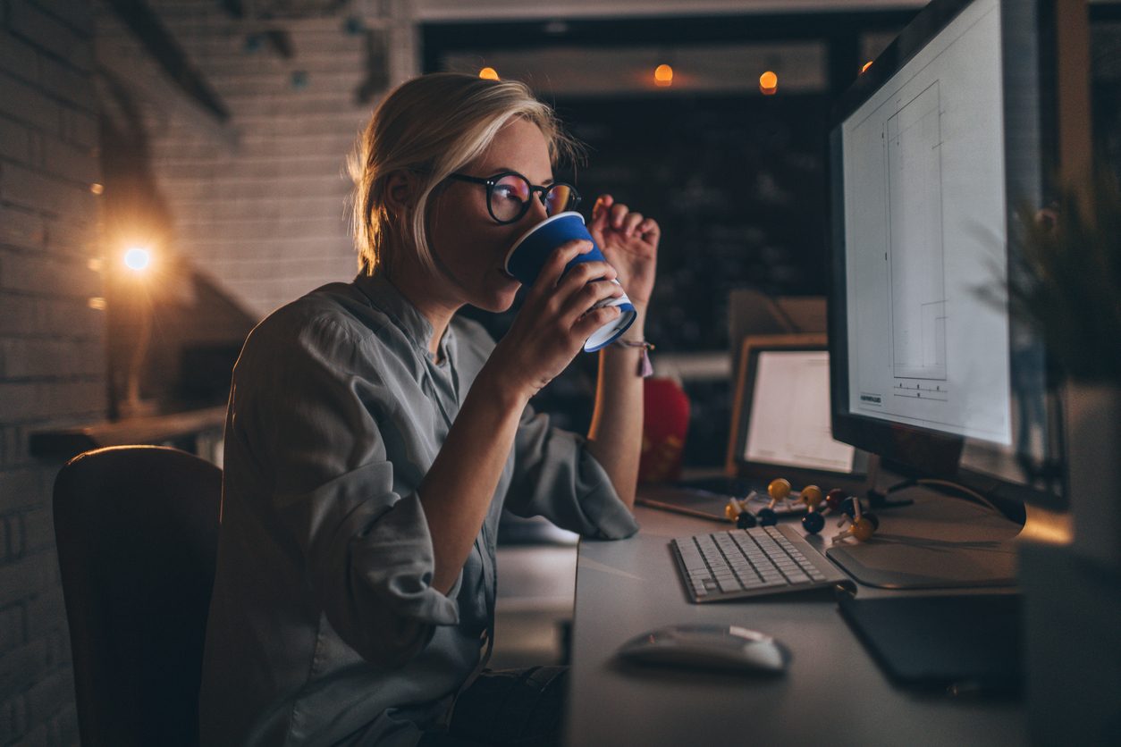 An worker at her computer at night, drinking coffee.