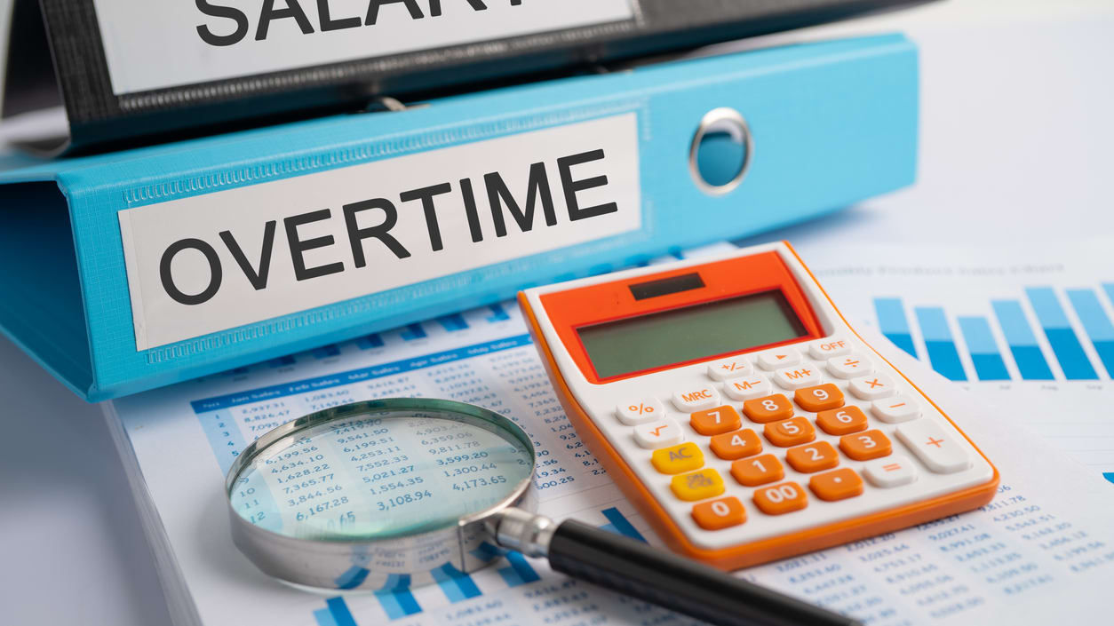 A magnifying glass and a folder with the words salary and overtime.