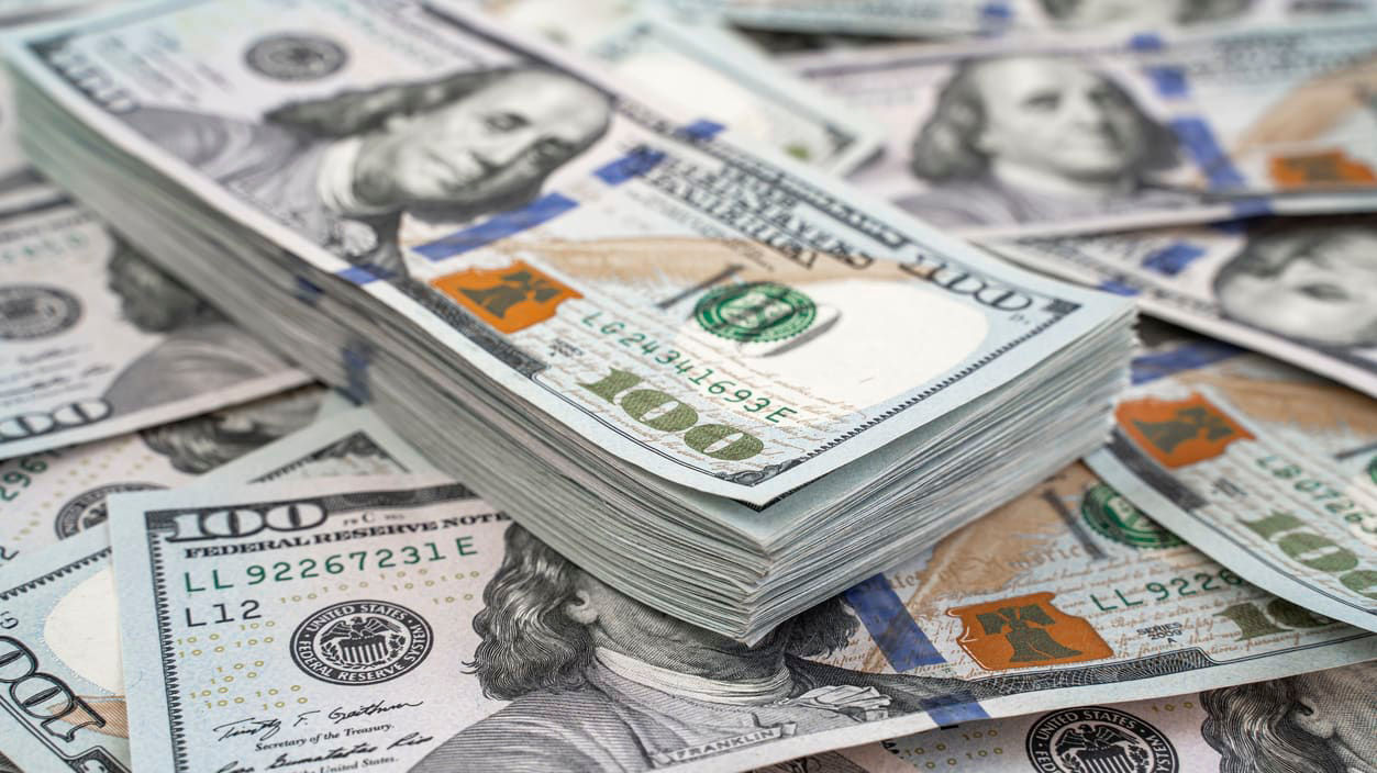 A pile of us dollar bills on a wooden table.