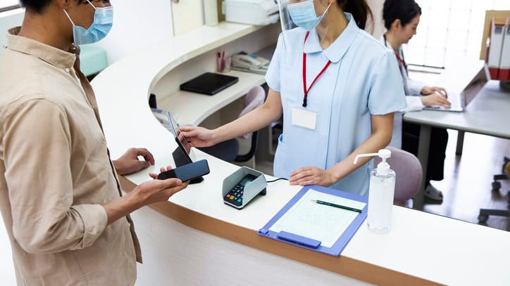A man wearing a face mask is standing at the front desk of a hospital.