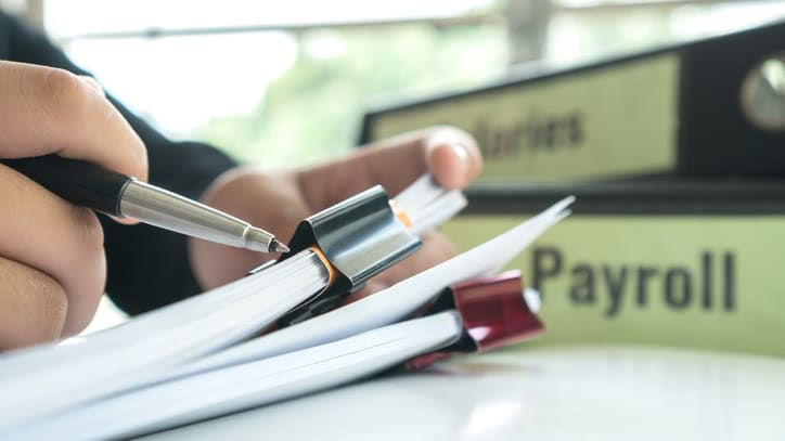 A person writing on a paper with the word payroll.