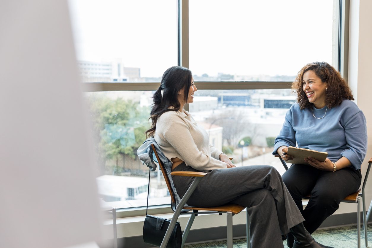 Two women sit by window in an office, discussing performance review