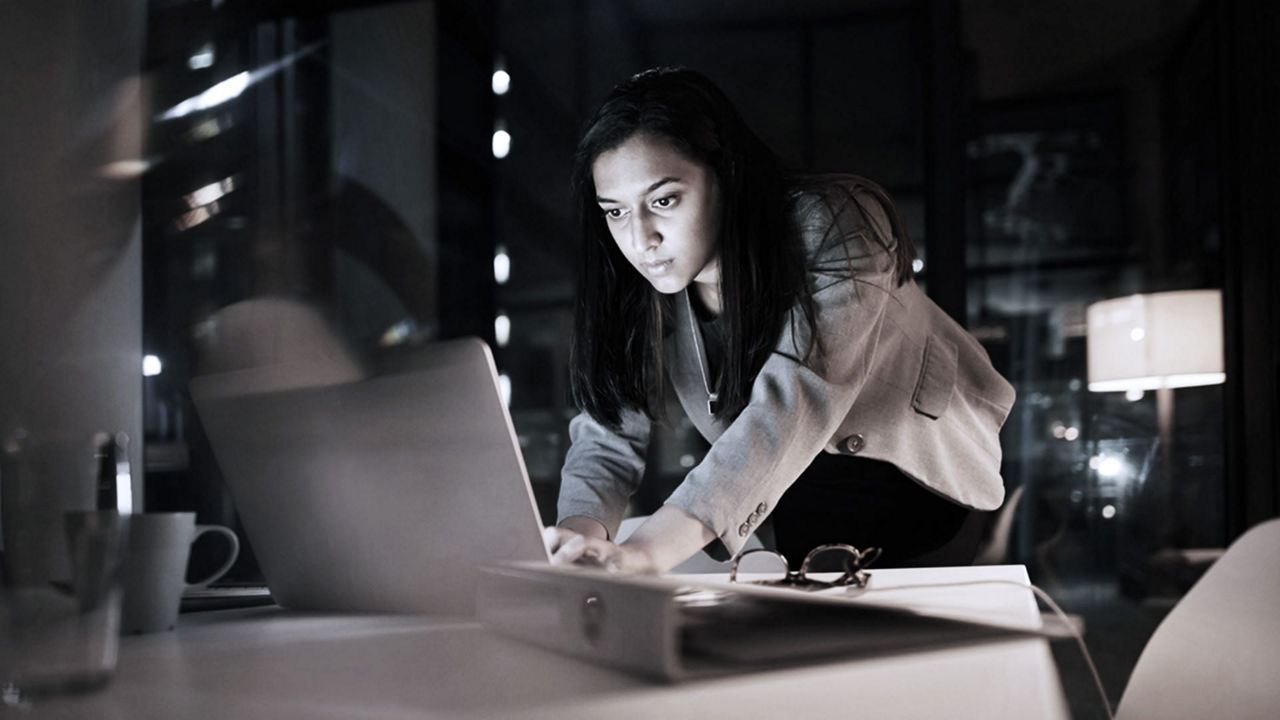 A woman working on a laptop in a dark room.