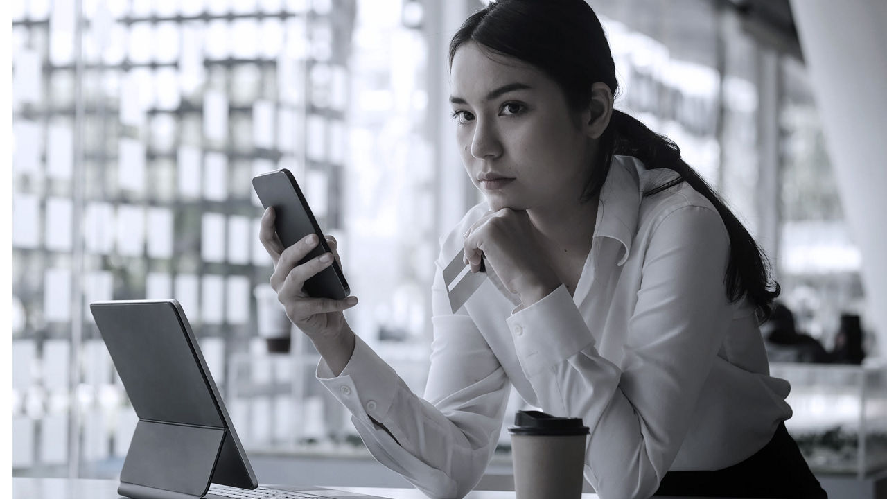 A woman sitting at a desk with a laptop and cell phone.