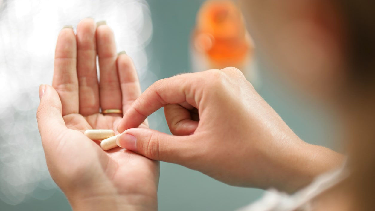 A woman is holding a pill in her hand.