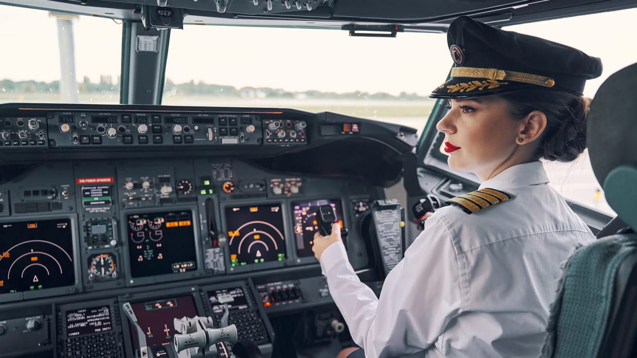 A female pilot is sitting in the cockpit of an airplane.
