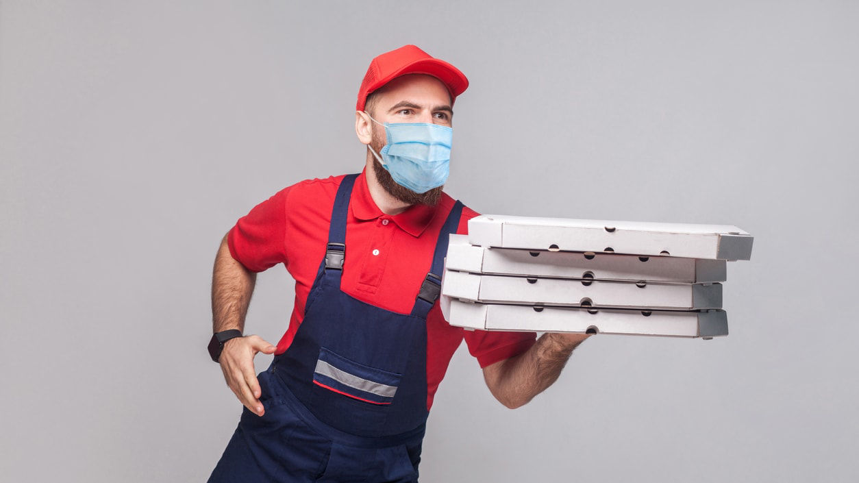 A pizza delivery man wearing a surgical mask and carrying pizza boxes.