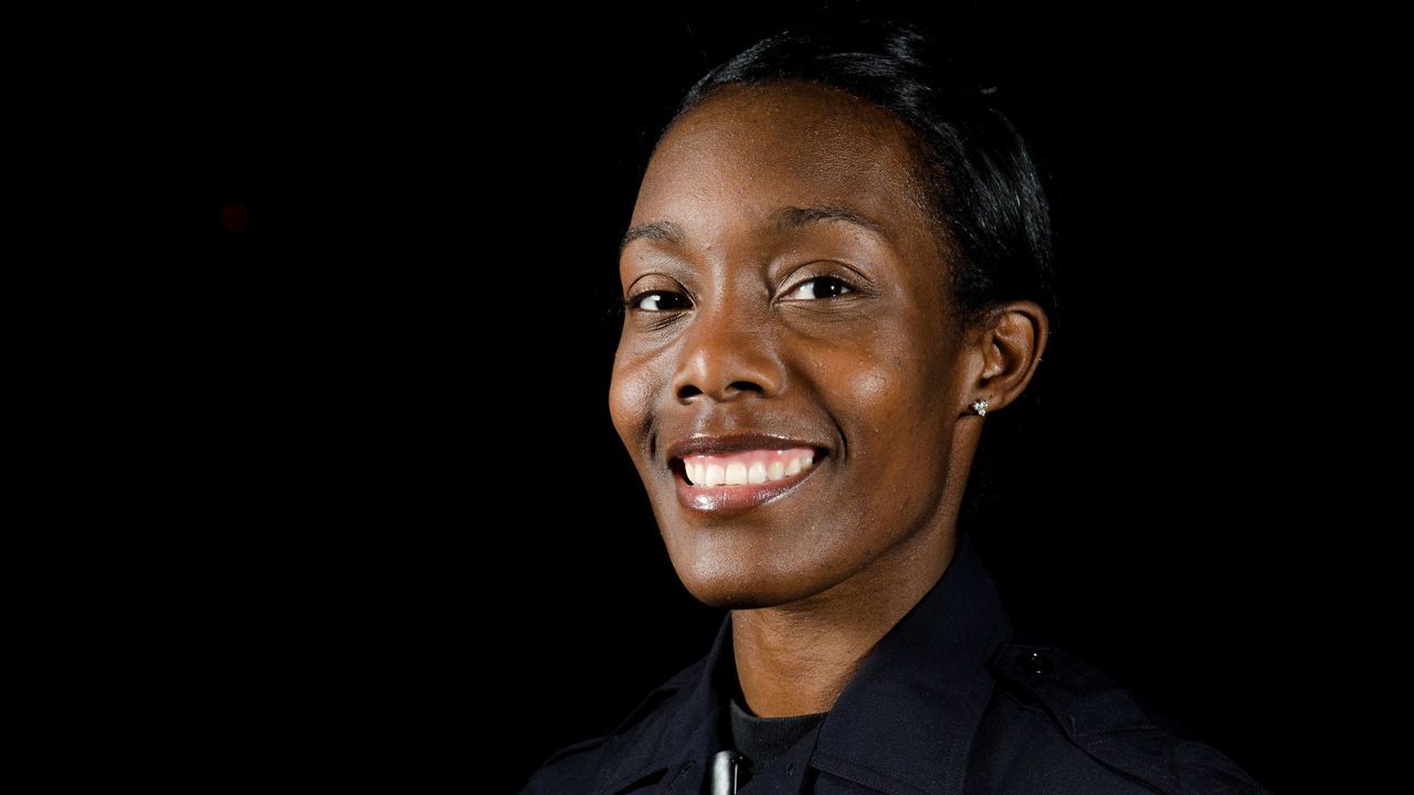 A female police officer smiling in front of a black background.